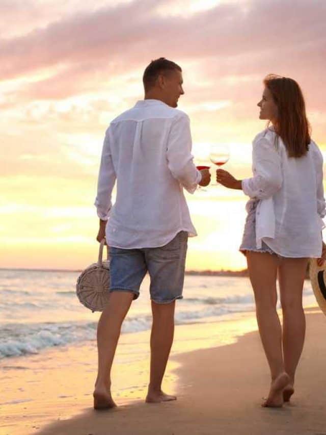 Lovely,Couple,With,Glasses,Of,Wine,Walking,On,Beach,At