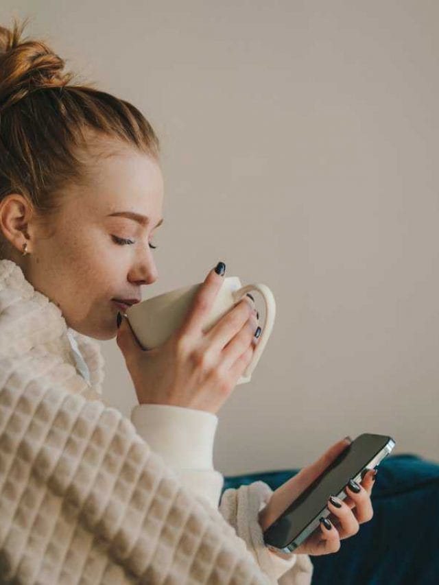 Relaxed,Young,Woman,Sitting,Under,Blanket,Using,Phone,And,Enjoying