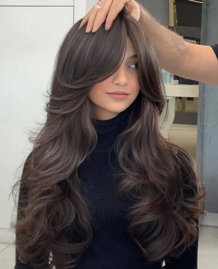 A woman with long wavy hair getting her hair styled by a professional hairdresser.
