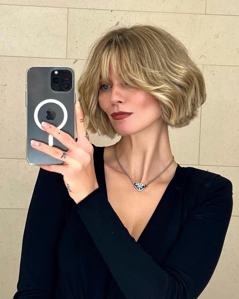 A woman with short blonde hair smiling while taking a selfie.