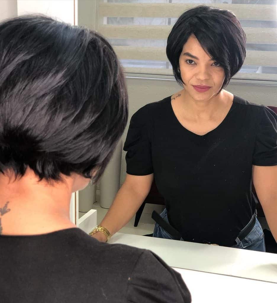 A woman with short black hair looking in the mirror.