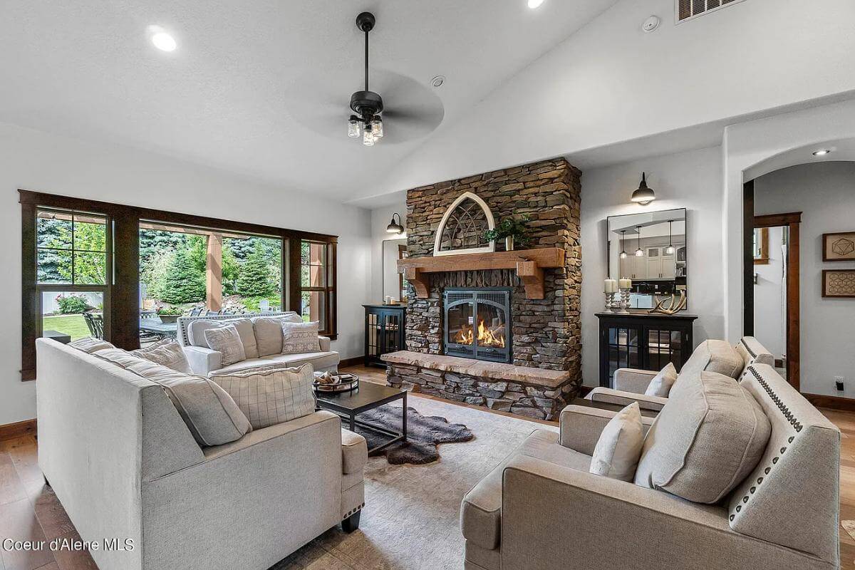 Living room with gray sofas, a stone fireplace, and an iron fan mounted on the vaulted ceiling.