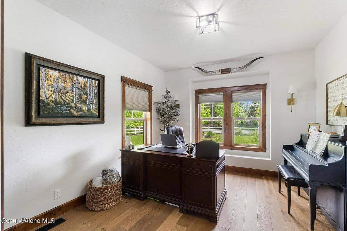 Office with a dark wood desk and an upright piano over the wide plank flooring.