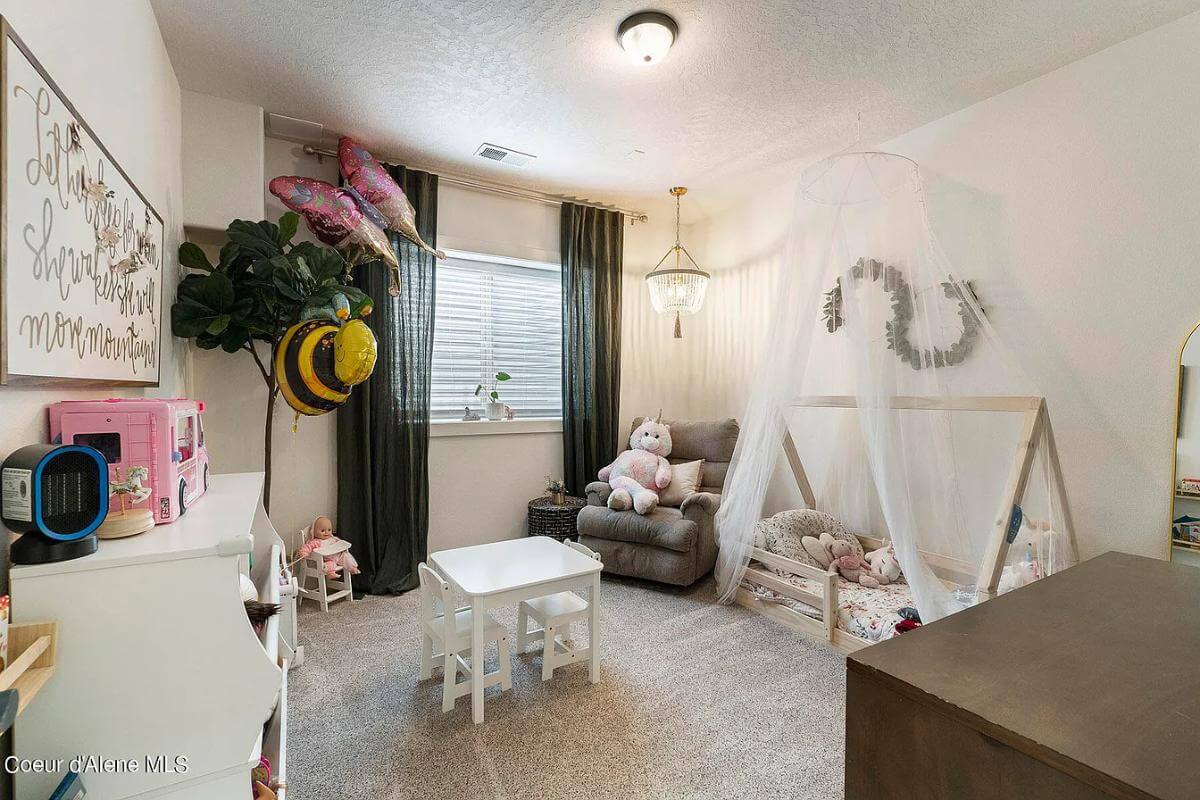 Kid's bedroom with a custom bed a cushioned chair, and a white table over the carpeted floor.