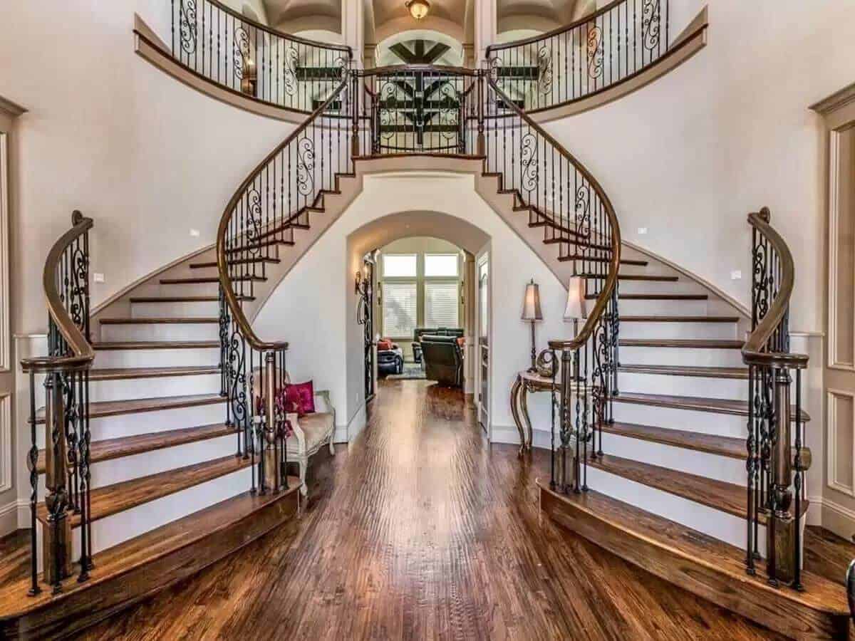 Foyer with a bifurcated staircase framed by intricate wrought iron railings.