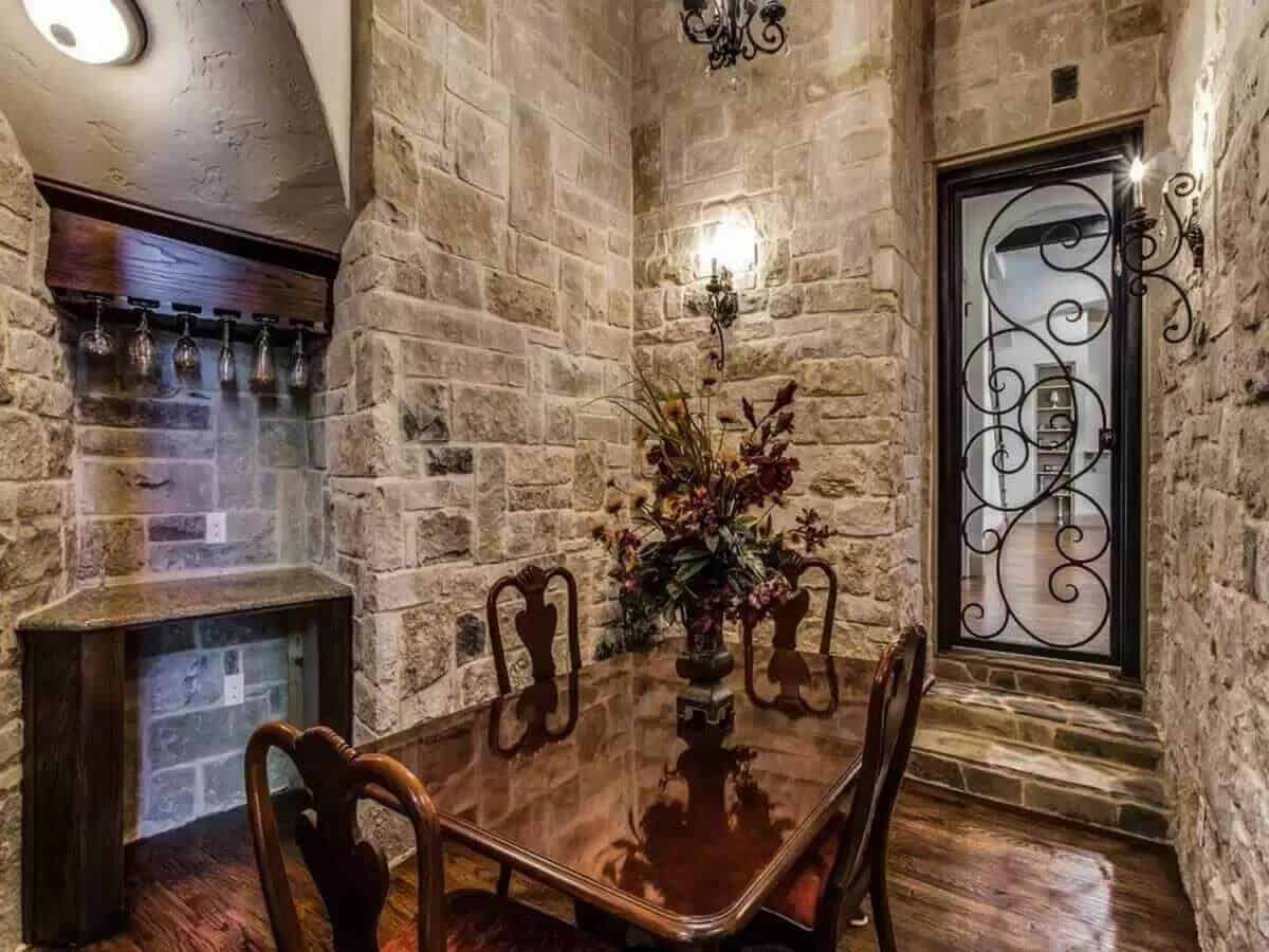 Wine cellar with stone walls, a wooden dining set, and a glazed door adorned by ornate detailing.