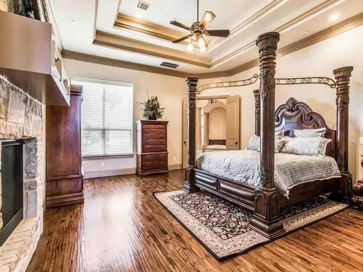 Primary bedroom with a stone fireplace and a four-poster bed crowned by a step ceiling.