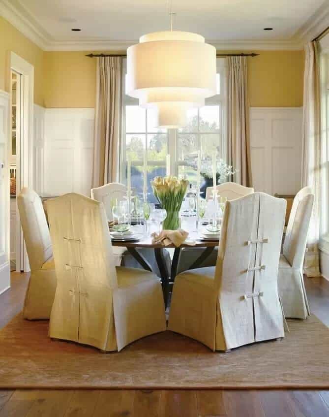 Dining room with a round table and skirted chairs illuminated by an oversized chandelier.