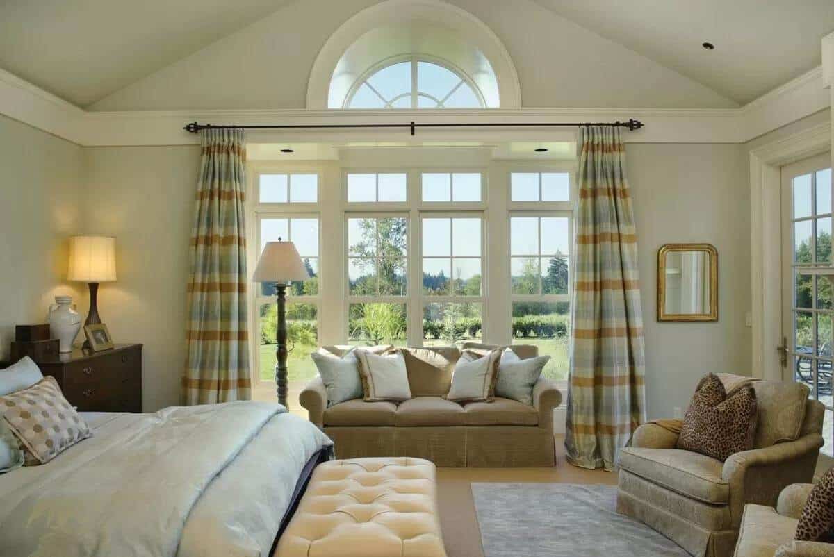 Primary bedroom with a tufted chair, skirted seats, and a Palladian window dressed in checkered drapes.