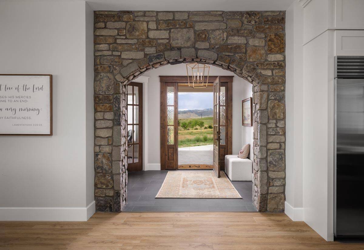 Foyer with a brick archway, a glazed front door, and white stools complemented with a rug.