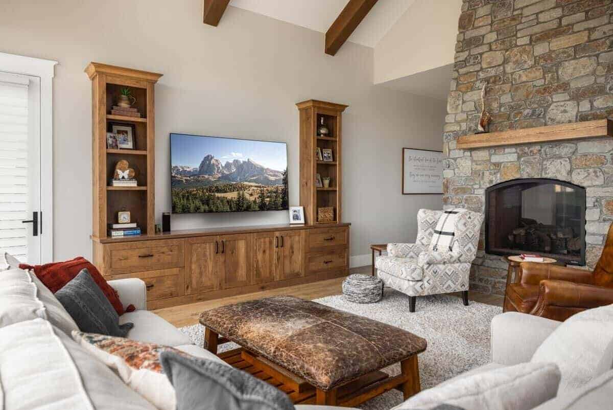 Family room with a stone fireplace, mismatched seats, and a wall-mounted TV surrounded by wooden cabinets.