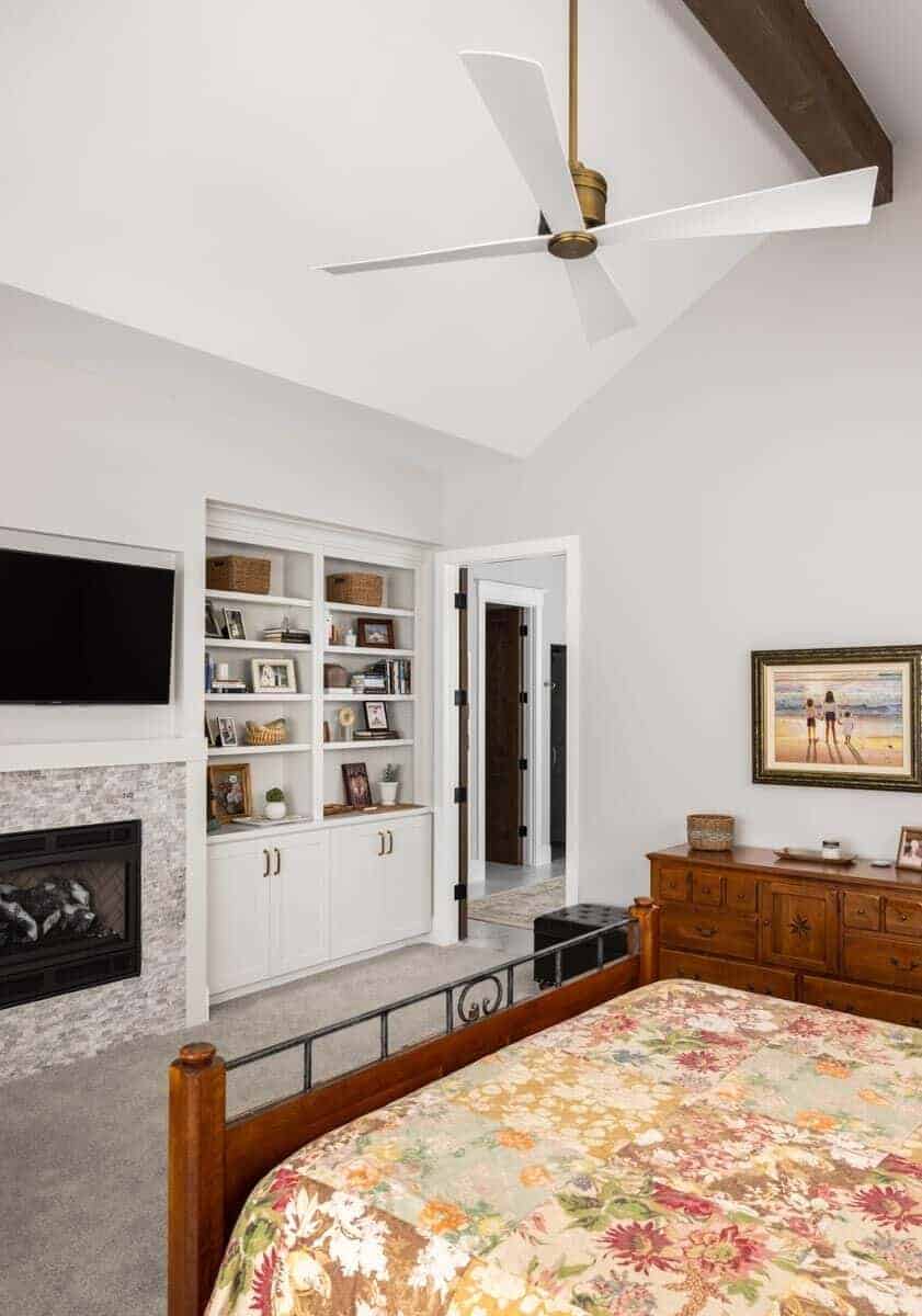 Primary bedroom with a vaulted ceiling, wooden furnishings, white built-ins, and a fireplace topped with a TV.