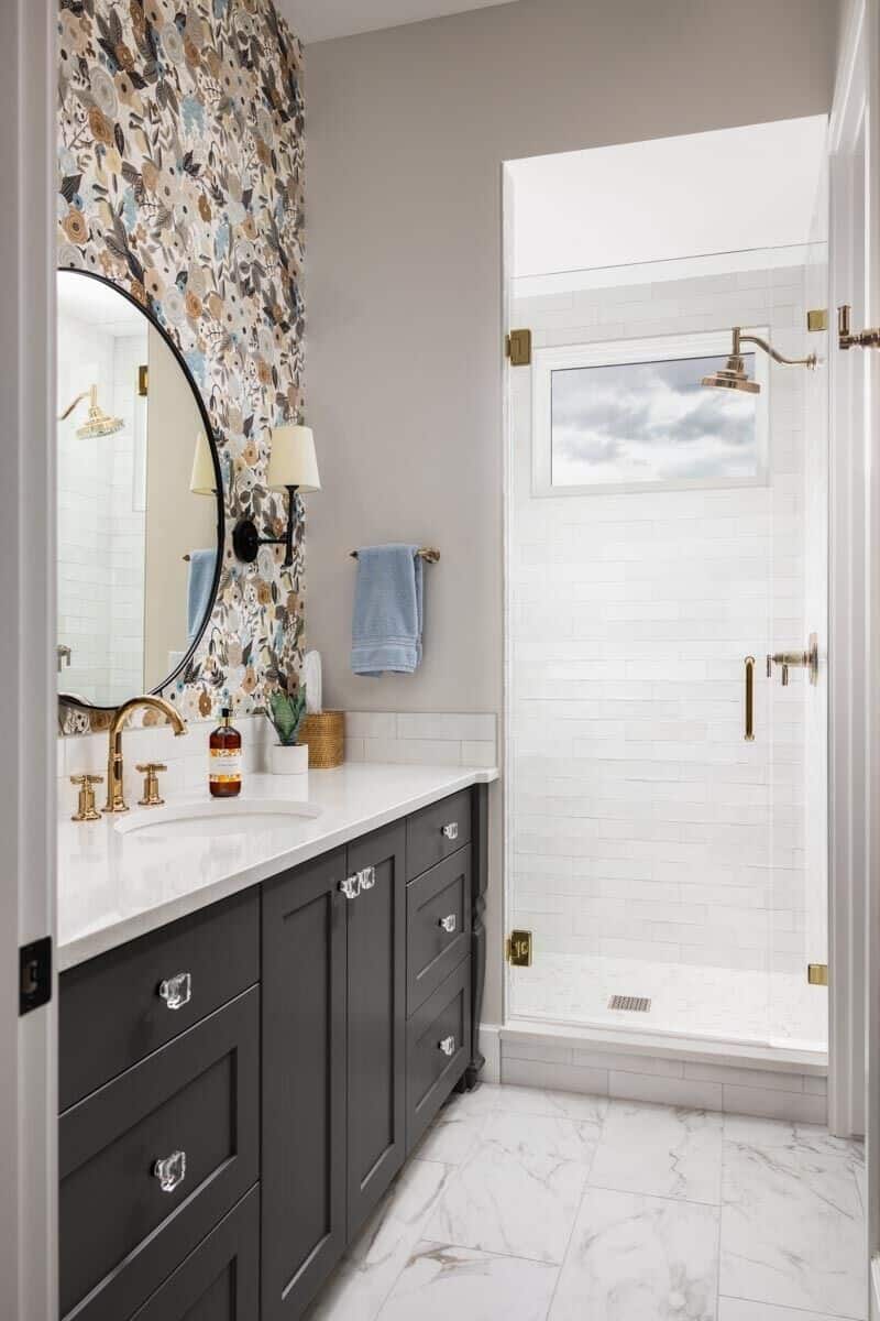 Bathroom with a walk-in shower and a black vanity adorned with floral wallpaper and round mirror.