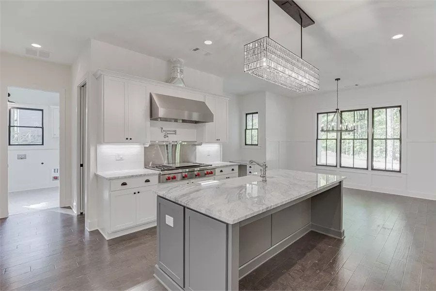 Kitchen with white cabinets and a breakfast island illuminated by a linear chandelier.