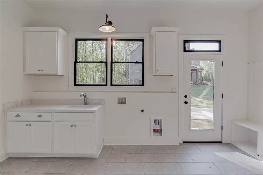 Laundry room with white cabinets, a utility sink, and outdoor access.