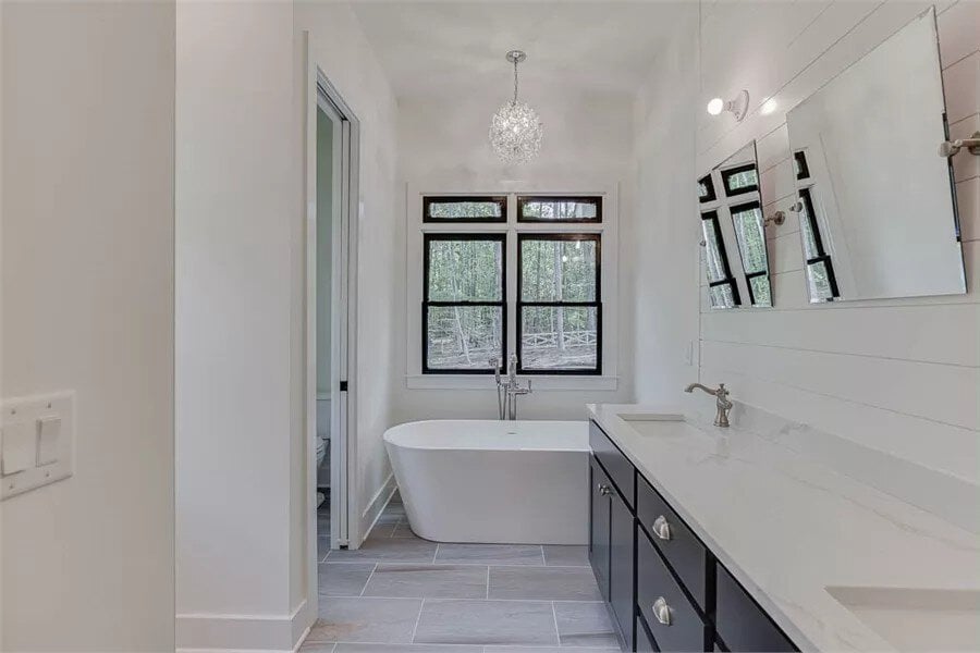 Primary bathroom with a dual sink vanity and a soaking tub under the framed windows.