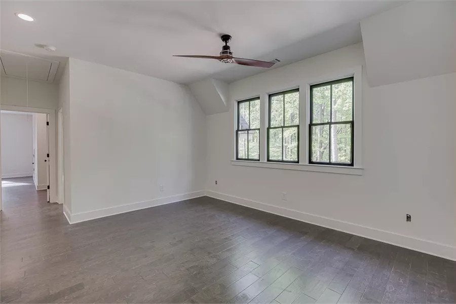 Loft with wide plank flooring and a trio of windows inviting natural light in.