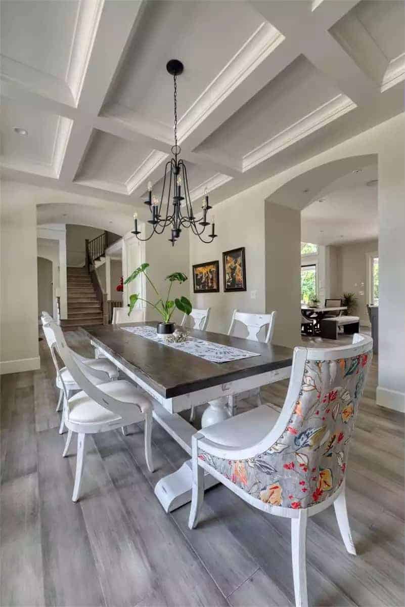 Dining room with white chairs and a rectangular dining table topped by a wrought iron chandelier.