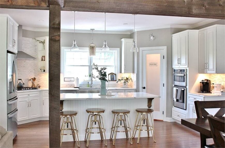 Rustic wood beams define the kitchen with white cabinetry stainless steel appliances, and a breakfast island bar.