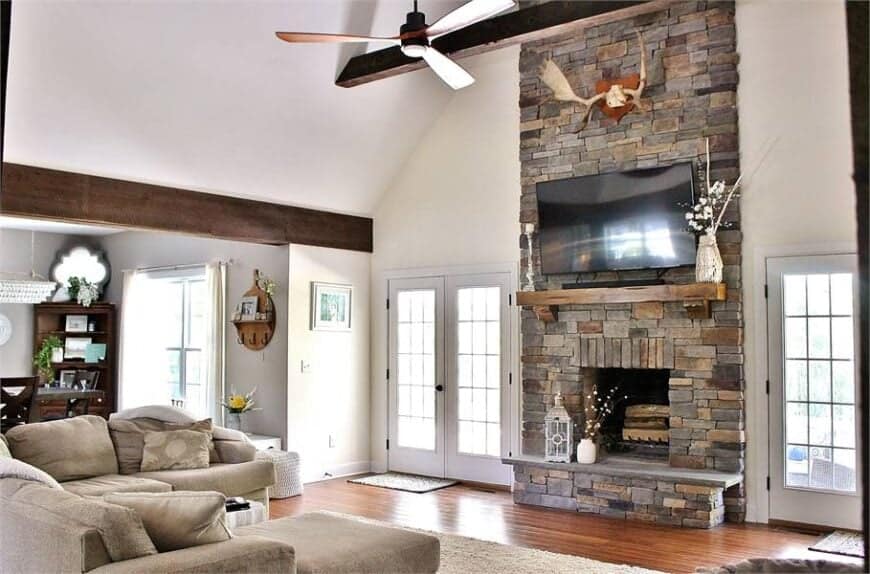 The living room offers beige seats, ceiling fan, and a stone fireplace with a wall-mounted TV on top.