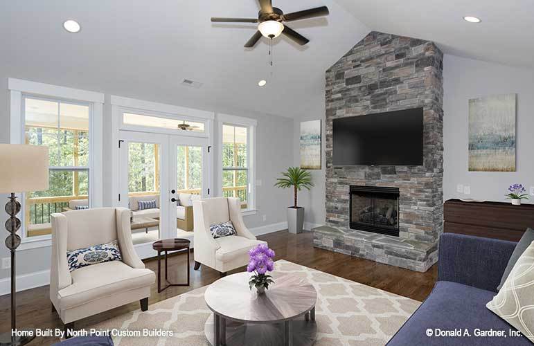 The living room has beige armchairs, a stone brick fireplace, blue sofa, and a round coffee table sitting on a patterned area rug.