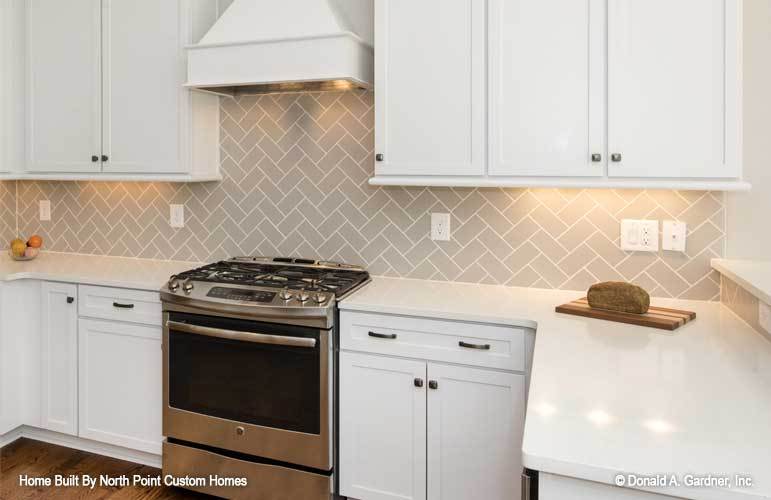 The kitchen offers a stainless steel range, white cabinetry, quartz countertops, and gray herringbone tile backsplash.