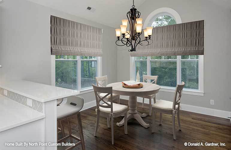 Breakfast nook with cushioned chairs and a round dining table illuminated by an ornate wrought iron chandelier.