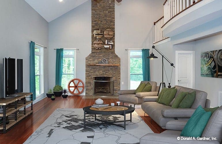 Living room with gray leather seats, a flatscreen TV, stone fireplace, and a round coffee table sitting on a printed rug.