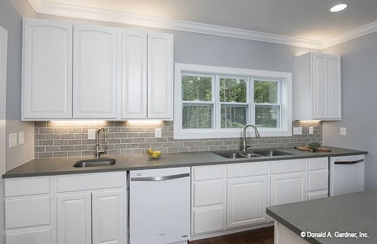 The kitchen is equipped with white appliances, custom cabinetry, gray subway tile backsplash, and undermount sinks.